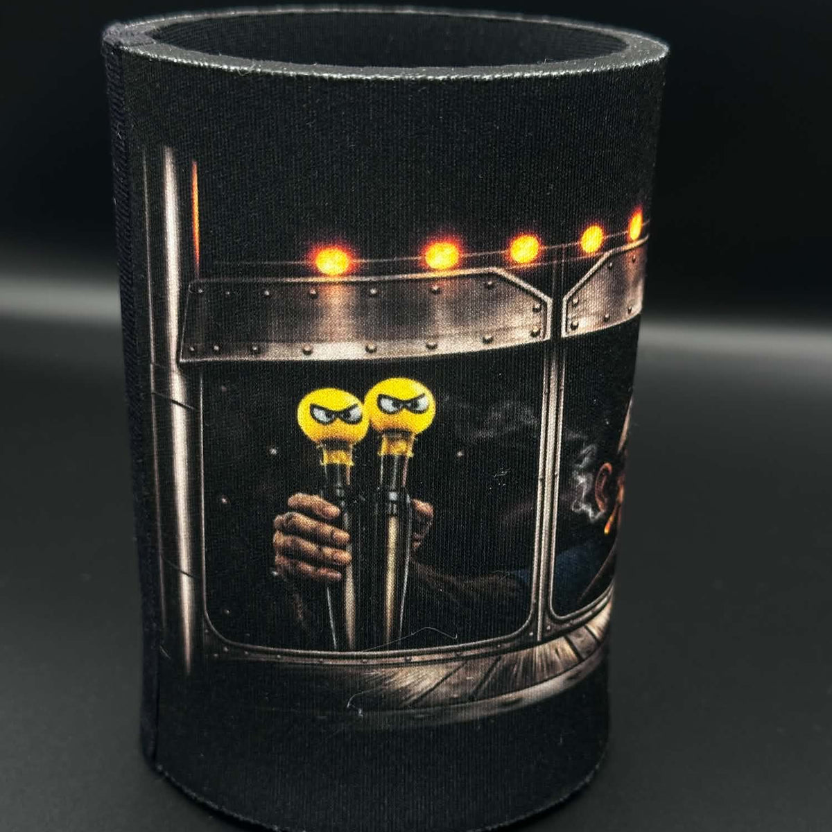 A black neoprene can cooler sleeve featuring a graphic print of a train window with yellow cartoon character toppers on the handles, set against a dark gray background.